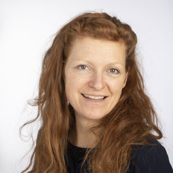 Dr Chloe Mortensen, a head and shoulders portrait of a woman with long red hair, smiling at the camera