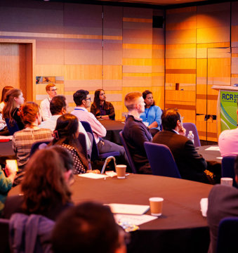 Group of attendees at the RCR 2023 conference listening to a speaker standing at a podium